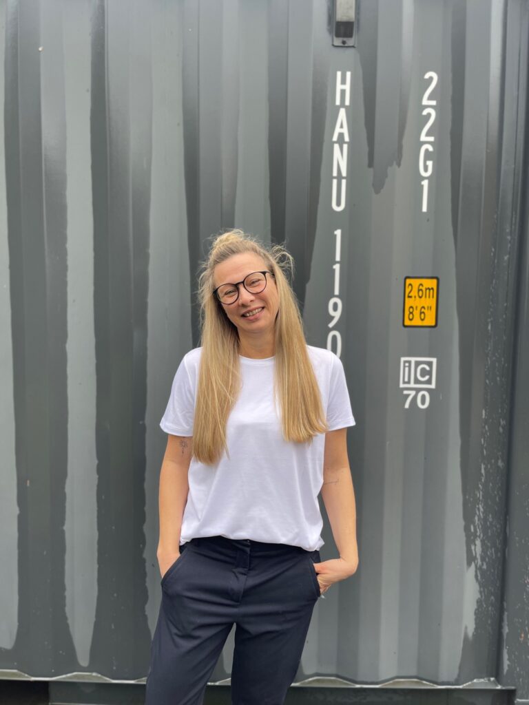 Führungskräfte Coach Anke Andresen steht vor einem grauen Container.